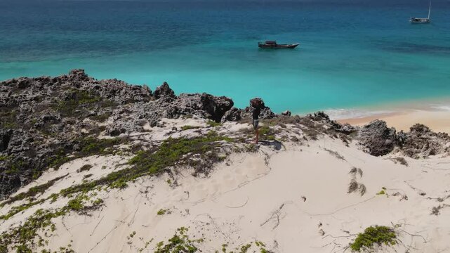 Male traveler exploring a desert island.Standing on a hill and looking into the distance of the Indian Ocean.Yaght at background