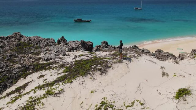 Male traveler exploring a desert island.Standing on a hill and looking into the distance of the Indian Ocean.Yaght at background