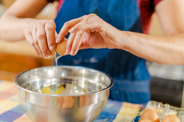 Chef cracking eggs into metal bowl for baking recipe