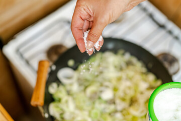 Chef adding salt to chopped leeks cooking in pan