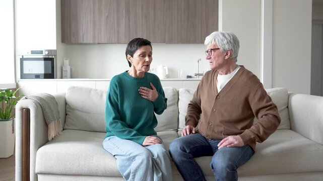 Mature woman suddenly feel heart distress, shortness of breath like asthma. Husband calming stroking, soothing wife on couch. Health scare, anxiety relief, overwhelming stress, deep concern of spouse