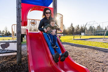 Mother and Child Sliding Down a Playground Slide in a Sunny Park