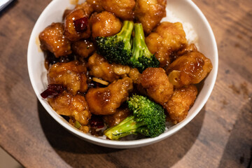 Delicious Asian-inspired dish with glazed chicken and vibrant green broccoli served in a white bowl on a wooden table. Flavorful food.