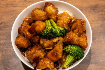 Bowl of savory fried chicken pieces with a shiny glaze and broccoli florets served atop white rice. Comfort food with rich umami flavor.