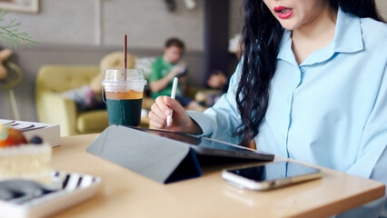 Business woman consultant motivation concept. A woman writing on a tablet in a cafe, with drinks and a smartphone on the table.