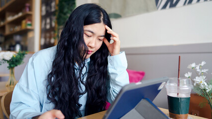 Obraz premium Business woman consultant motivation concept. A young woman with long hair appears stressed while using a tablet in a cozy cafe setting.