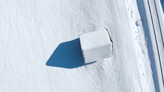 Aerial: zenital shot of a snowy cabin in the Alps, descending shot