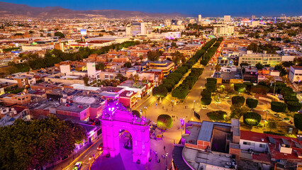 Naklejka premium Aerial view of the city of Leon at sunset. The Triumphal Arch of the Calzada de los Heroes is illuminated with vivid colors.
