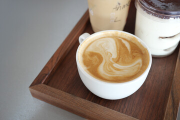 Warm coffee cup with swirling foam on a wooden tray