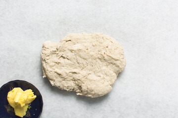 Top view of butter being mixed into bun dough on a marble countertop, Overhead view of hot cross bun dough being kneaded, process of making hot cross bun