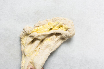 Top view of butter being mixed into bun dough on a marble countertop, Overhead view of hot cross bun dough being kneaded, process of making hot cross bun