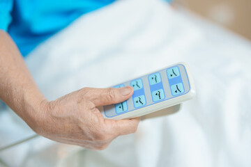 Elderly asian Woman patient hand using remote control for adjust level bed in hospital room. Happy Senior illness resting on comfortable electric bed in modern hospital