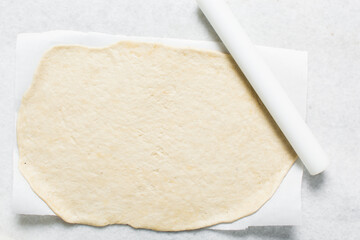 Overhead view of rolled out crackers dough on parchment paper, cracker biscuit dough on white background, process of making crackers