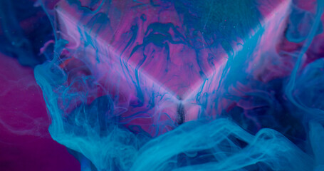 Ink mix. Art smoke. Blue color dye flow spill down pink purple fluorescent glass cube surface. Oil...