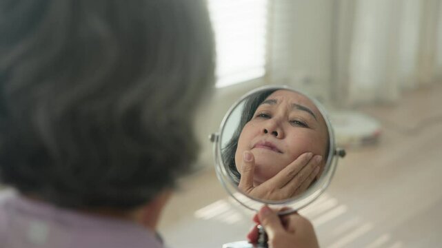 Asia adult people middle age old woman look at mirror dry skin face hand touch neck cheek stress sad at home elder health care aging beauty issue. Asian female aged eye botox filler plastic surgery.