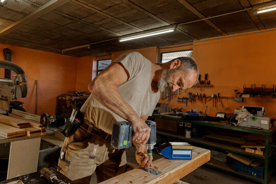 Carpenter using a power drill to assemble wooden parts in a workshop.