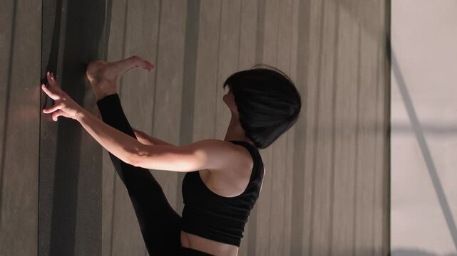 Vertical video. Stretch workout. Sport motivation. Flexible woman in activewear leaning forward leg gymnastic split exercise muscle warm-up on yoga mat in gym fitness studio indoors.