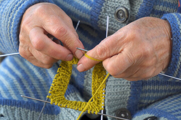 Elderly woman knits a sock with knitting needles and wool thread
