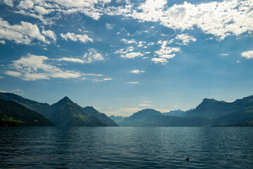 Alps mountain background. Swiss Alps mountain on sunny day. Mountain under clouds in blue sky. Blue nature background. Blue lake with blue sky near mountain.