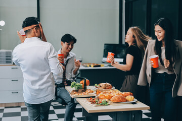 Asian office colleagues and friends enjoy a daytime BBQ with pizza and beer, celebrating Halloween and cheering for their favorite soccer team, creating a lively atmosphere filled with joy.