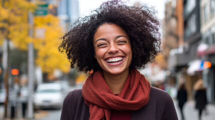 Fototapeta premium joyful woman with curly hair smiles brightly in urban setting, surrounded by autumn foliage.