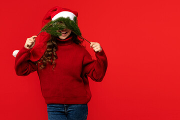 Teen girl in Santa hat playfully covering her face with fir branches