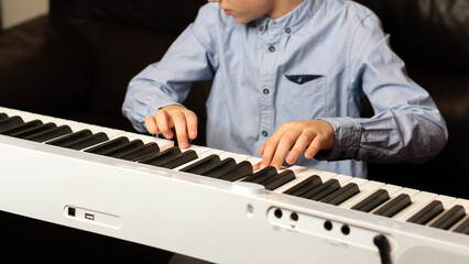 Child boy playing the keyboard with focused hands and fingers. Practicing piano at home