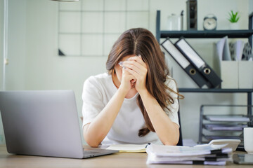 A woman is sitting at a desk with a laptop and a stack of papers