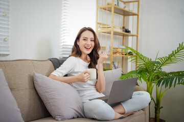 A woman is sitting on a couch with a laptop and a cup of coffee