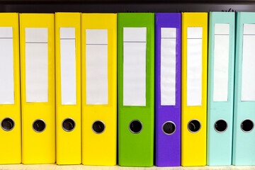 Many colorful folders with documents on the shelves of the cabinet in the office.	