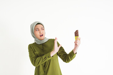 young woman dressed casually in a green outfit with a hijab shows an expression of dislike or...