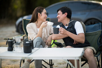 A woman and man is smiling at each other while holding their cup at folding table on camping ground