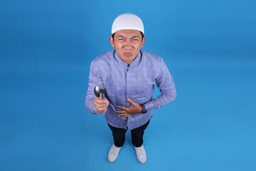 Top View Of Young Muslim Man Hungry While Holds Spoon And Fork Waiting Breakfasting Time On Blue...
