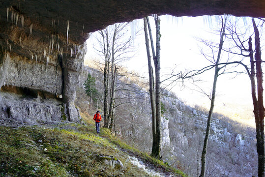 Visiting interesting locations in the mountains on the Montenegrin coast: a tourist in the Fairy Cave (Vilina pecina) in the Orjen Nature Park. Landscape with a cave ceiling, a forest and a man.