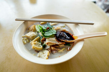 Close up of a bowl of curry mee or noodle in thick spicy gravy soup which is popular in Malaysia and Singapore. Toppings include cuttlefish, cockles, tofu and cogulated pig blood.