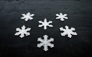 Five white snowflake shapes arranged on a dark gray textured background.  The snowflakes vary slightly in size and are the central focus of the image