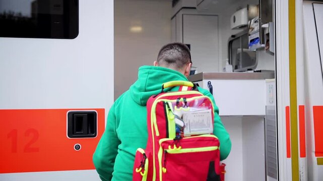 Paramedic wearing green jacket standing next to an open ambulance vehicle, carrying a medical emergency backpack, ready for duty. Emergency response, medical care, and healthcare services in action
