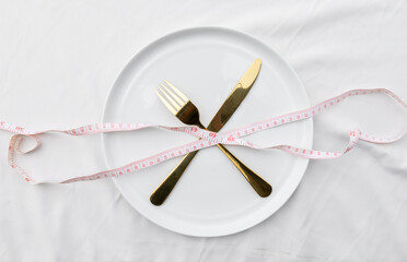 An empty ceramic plate wrapped with a waist measurement tape, symbolizing diet, nutrition, and healthy lifestyle planning.