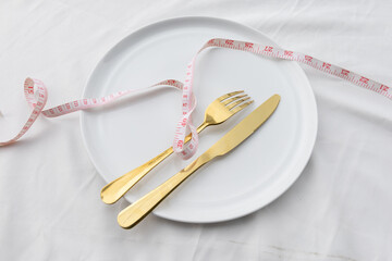 An empty ceramic plate wrapped with a waist measurement tape, symbolizing diet, nutrition, and...