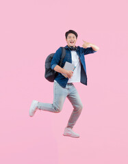 Full body image of young Asian male student holding book , wear backpack and running on pink background	