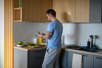 Diabetic man with CGM sensor checking his blood sugar level while making healthy breakfast.