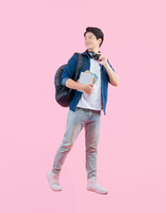 Full body image of young Asian male student holding book , wear backpack and posing on pink...