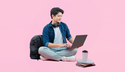 Full body image of young Asian male student using laptop and posing on pink background