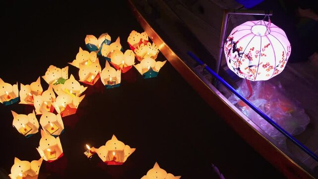 Floating lanterns illuminate the dark waters during a traditional festival in Vietnam. A beautifully decorated boat with a glowing lantern adds to the magical and serene atmosphere.