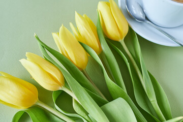 Naklejka premium Bouquet of yellow tulips and a cup of coffee on a green background
