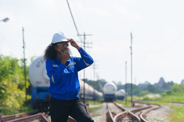 Female and male engineers work under the hot sun on an oil tanker train in an industrial plant.