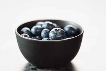 Ripe blueberries in black bowl on concrete background closeup