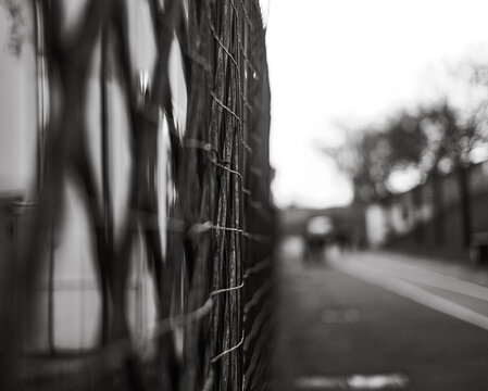 Fototapeta Blurred street view through a metal fence, capturing depth with selective focus in soft monochrome tones.