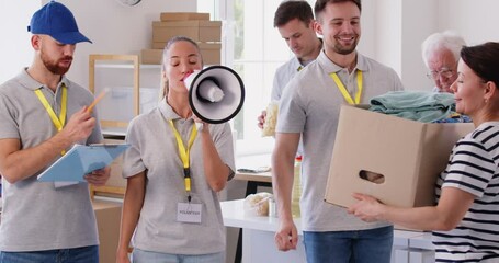 Volunteers are working together to organize donation drive at local warehouse. One female volunteer is using megaphone to announce something, while another man is holding clipboard and writing.