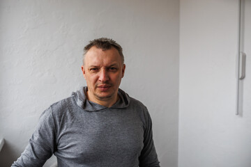 Portrait of a cheerful middle-aged man wearing a gray hoodie, standing against a textured stone...